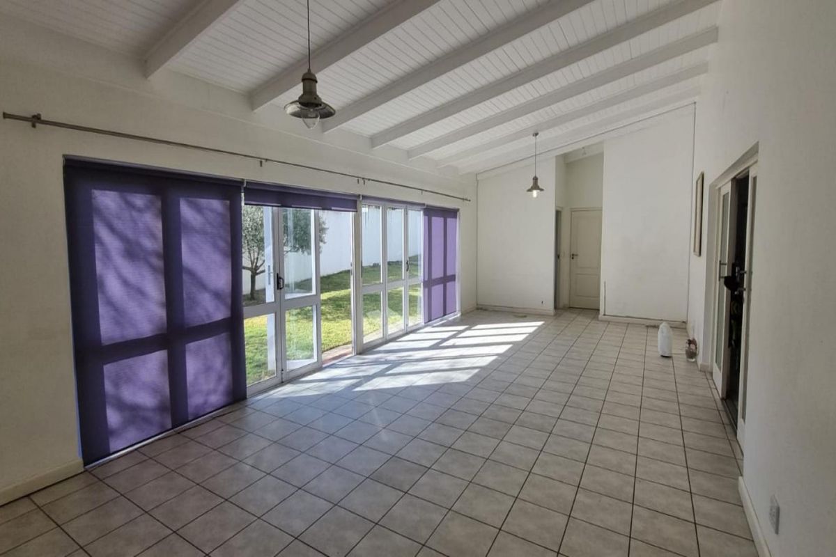 Spacious, light-filled living area featuring tiled floors, exposed beam ceilings, and large glass sliding doors providing direct access to the garden.