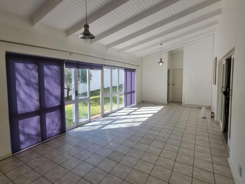 Spacious, light-filled living area featuring tiled floors, exposed beam ceilings, and large glass sliding doors providing direct access to the garden.