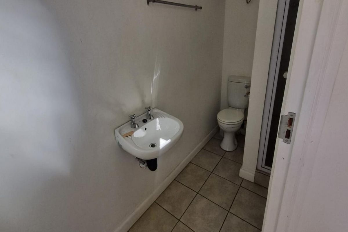A functional bathroom featuring a wall-mounted basin, toilet, and tiled flooring, presenting a clean and simple layout.