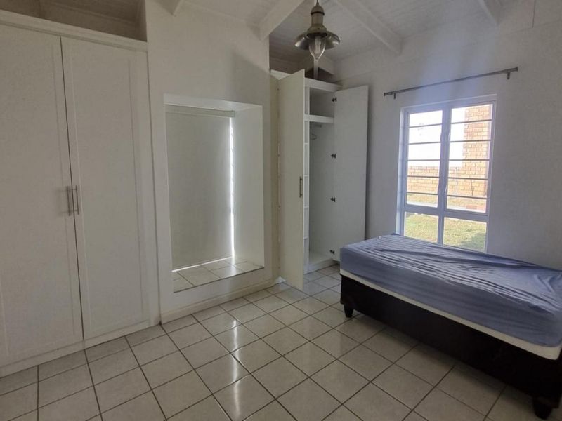 A bedroom featuring tiled flooring, built-in cupboards, and an exposed beam ceiling with natural light from the window.