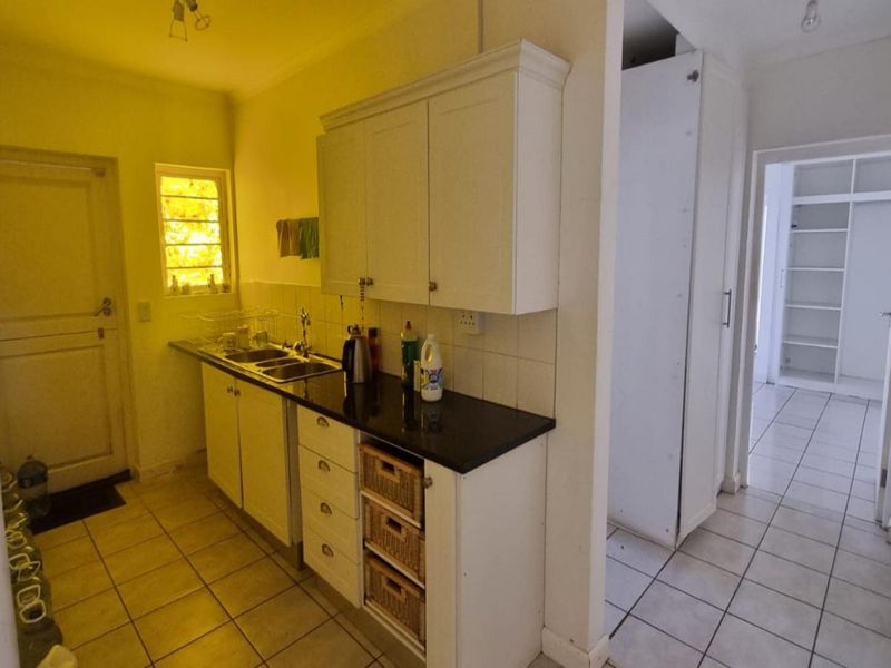 A functional scullery area featuring built-in cabinetry, a double sink, stone countertops, and tiled flooring, with an adjacent storage or pantry space.