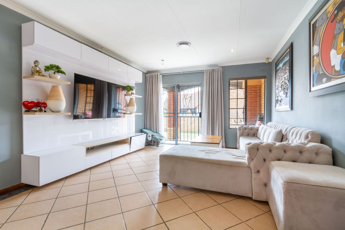 A well-maintained living room featuring a modern built-in media unit, tiled flooring, and direct access to an outdoor area through a sliding security door.