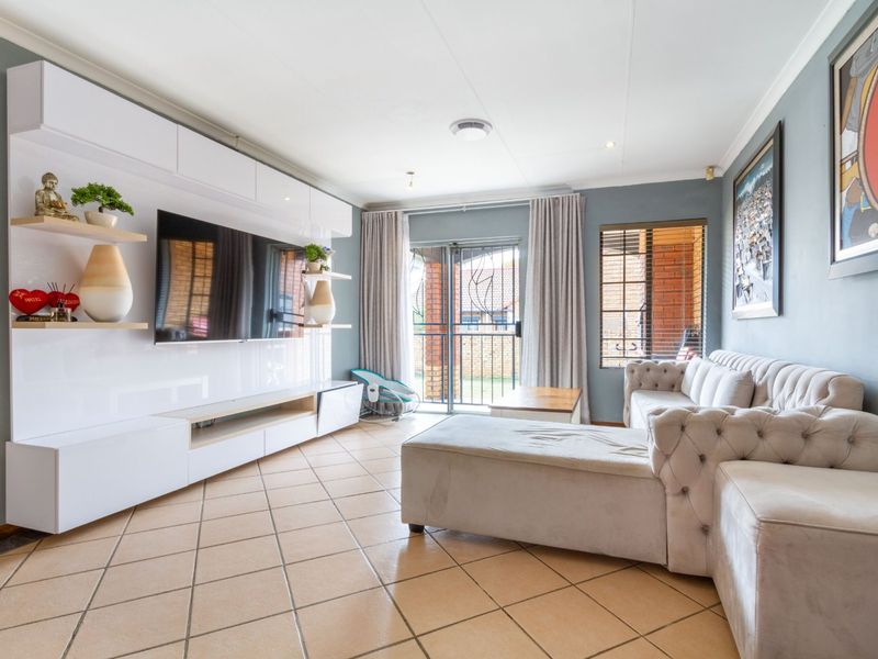 A well-maintained living room featuring a modern built-in media unit, tiled flooring, and direct access to an outdoor area through a sliding security door.
