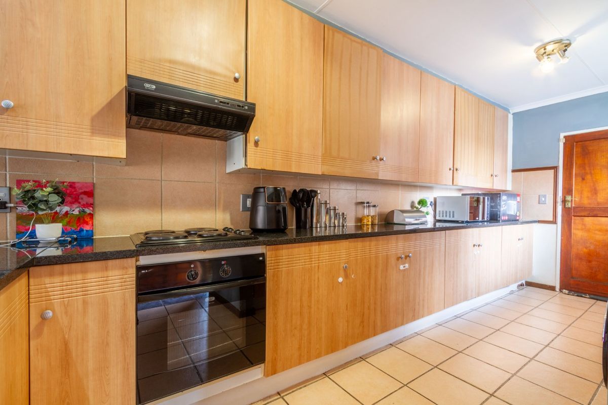 A functional kitchen featuring light wood cabinetry, granite countertops, a built-in oven, gas hob, and tiled flooring with a neutral backsplash.