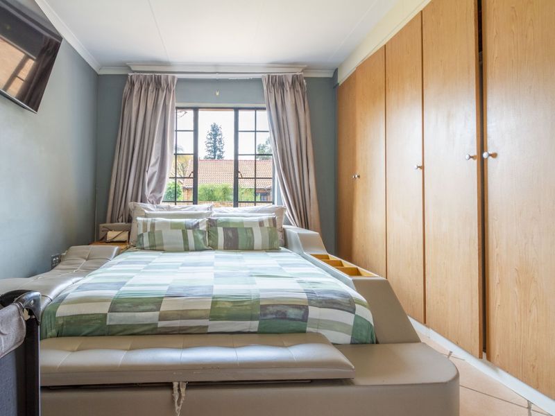 A bedroom featuring built-in wooden cupboards, tiled flooring, and a steel-framed window providing natural light.
