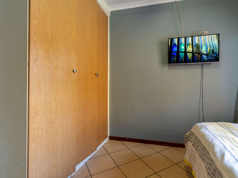 A bedroom featuring a built-in wooden wardrobe, tiled flooring, and a wall-mounted television.