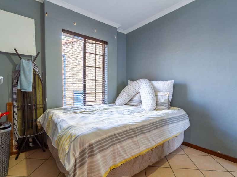 A compact bedroom featuring tiled flooring, a sliding window with venetian blinds, and coved ceiling detailing.