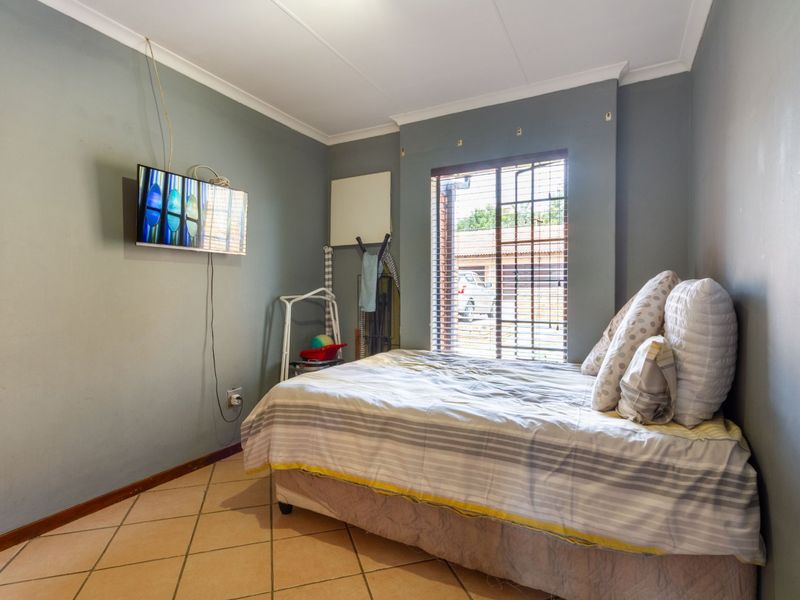 A bedroom featuring tiled flooring, cove cornicing, and venetian blinds, providing a functional space with neutral wall tones.