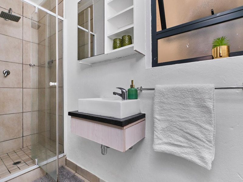 A modern bathroom featuring a glass-enclosed shower with a rain shower head, a wall-mounted vanity with a vessel sink, and a mirrored medicine cabinet.