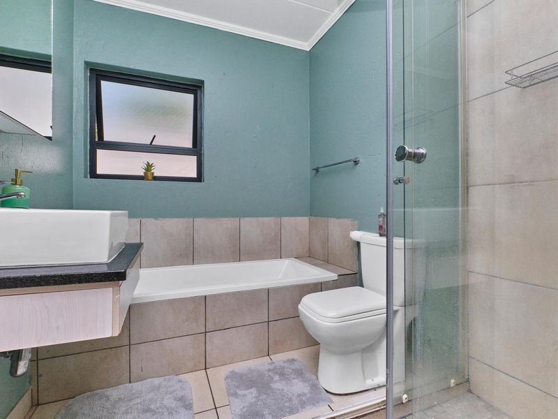 A functional bathroom featuring a built-in bathtub, separate glass shower enclosure, vessel sink vanity, and toilet with neutral wall and floor tiling.