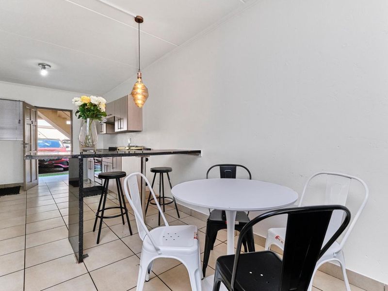 Open-plan kitchen and dining area featuring tiled flooring, a granite breakfast bar, and integrated laundry space with direct exterior access.