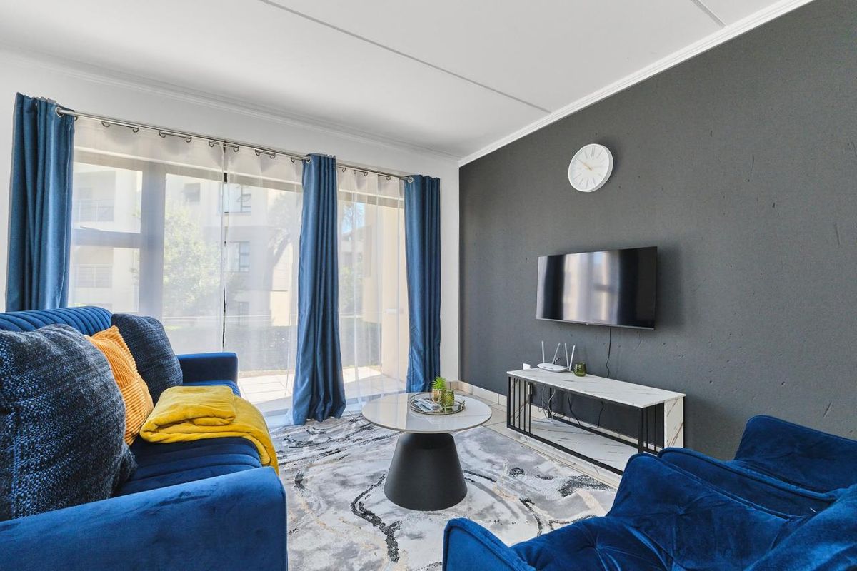 A well-maintained living room featuring tiled flooring, a dark accent wall, and large sliding glass doors that provide ample natural light.