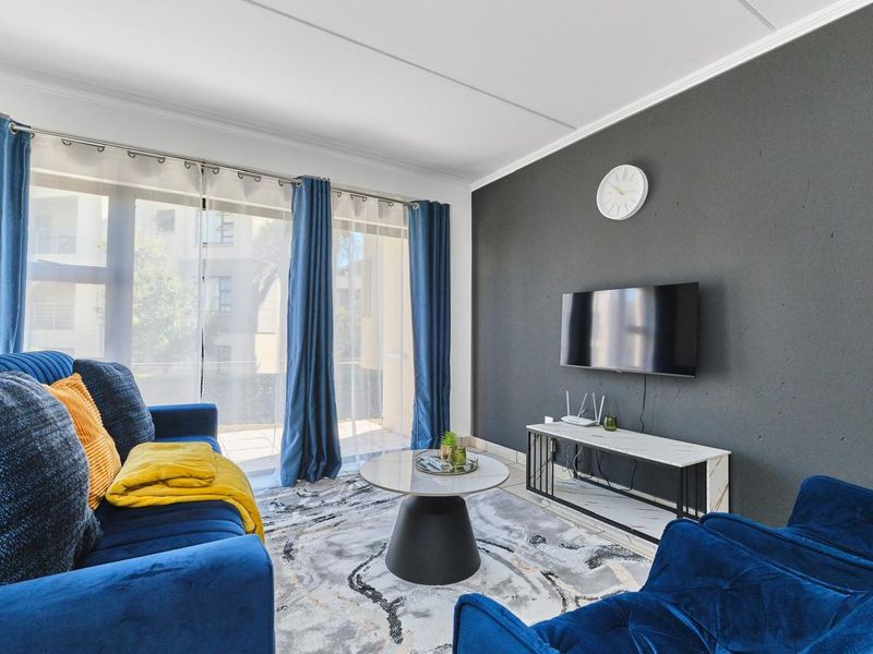 A well-maintained living room featuring tiled flooring, a dark accent wall, and large sliding glass doors that provide ample natural light.