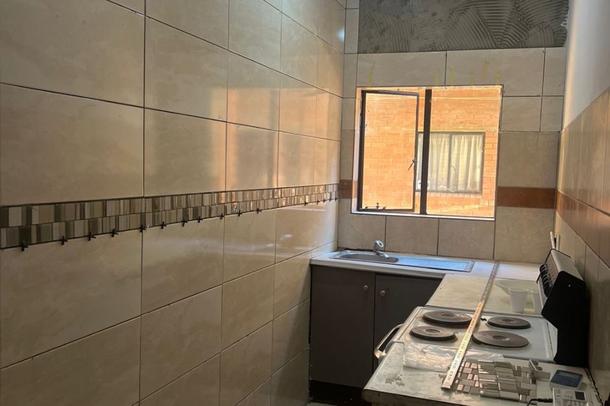 A kitchen space currently undergoing renovation, featuring tiled walls, a sink, and an electric stove, requiring finishing touches to complete the installation.