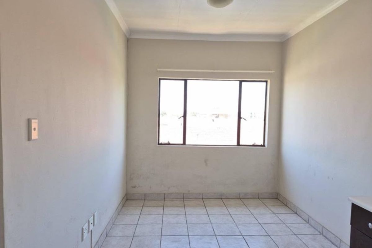 An empty bedroom featuring tiled flooring, neutral walls, and a window, providing a blank canvas ready for personalization.