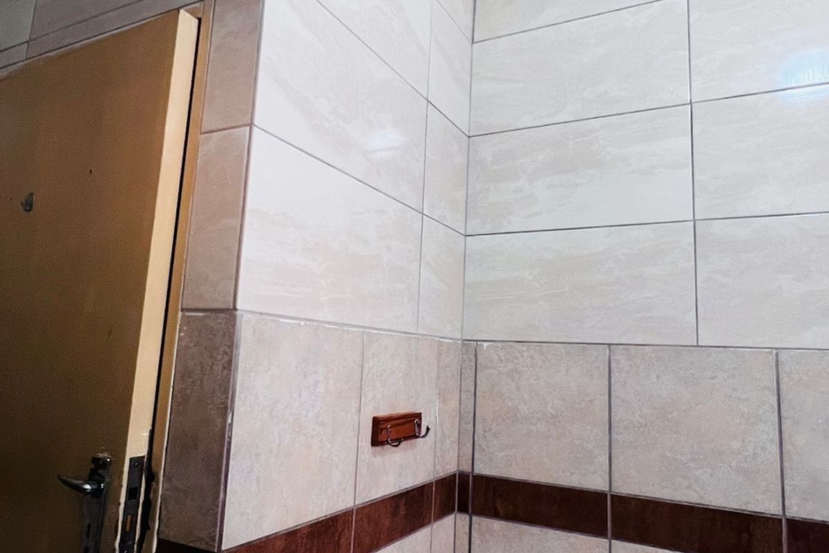 A bathroom corner featuring ceramic wall tiles, a shower tray, and a towel hook, requiring ceiling finishing and door frame repairs.