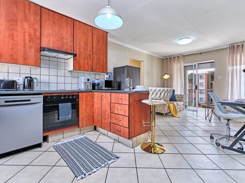Open-plan kitchen and living area featuring wood-finish cabinetry, tiled flooring, and direct access to a balcony through sliding glass doors.