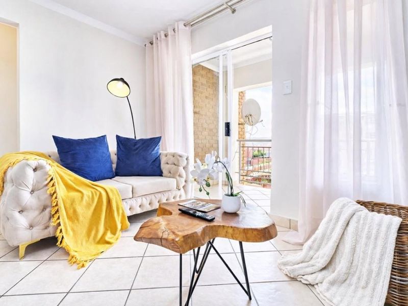 A bright living room featuring tiled flooring and a sliding glass door that provides access to an outdoor balcony area.