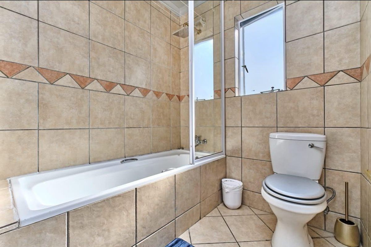 A functional bathroom featuring a built-in bathtub with a glass shower screen, tiled walls, and a standard toilet.
