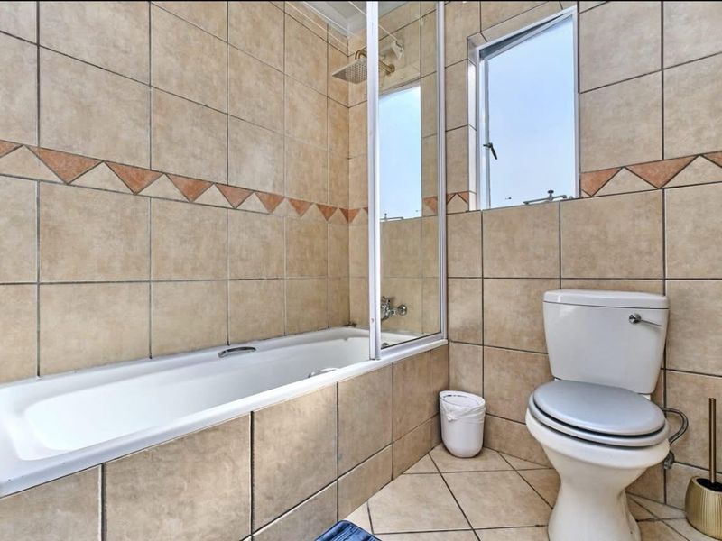 A functional bathroom featuring a built-in bathtub with a glass shower screen, tiled walls, and a standard toilet.