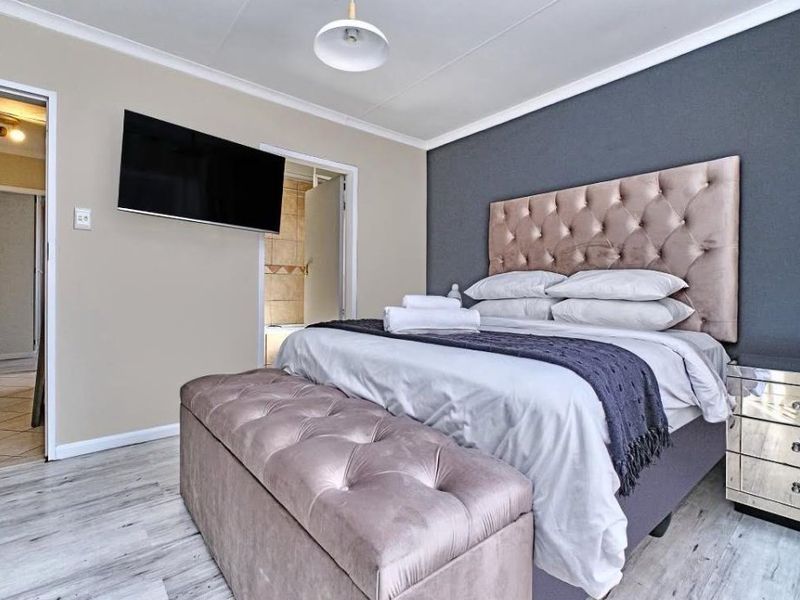 A well-maintained bedroom featuring light laminate flooring, a dark grey accent wall, and coving detail, with an adjoining bathroom visible through the doorway.