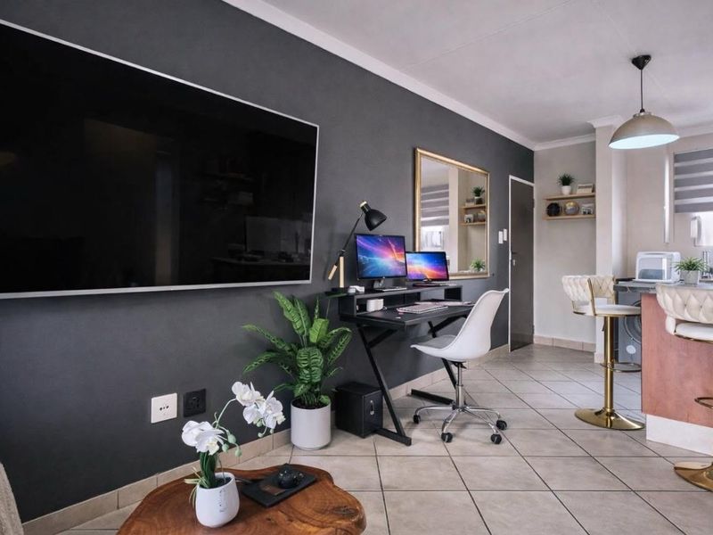 Modern open-plan living area featuring tiled flooring, a dark accent wall, and a functional kitchen breakfast bar with pendant lighting.
