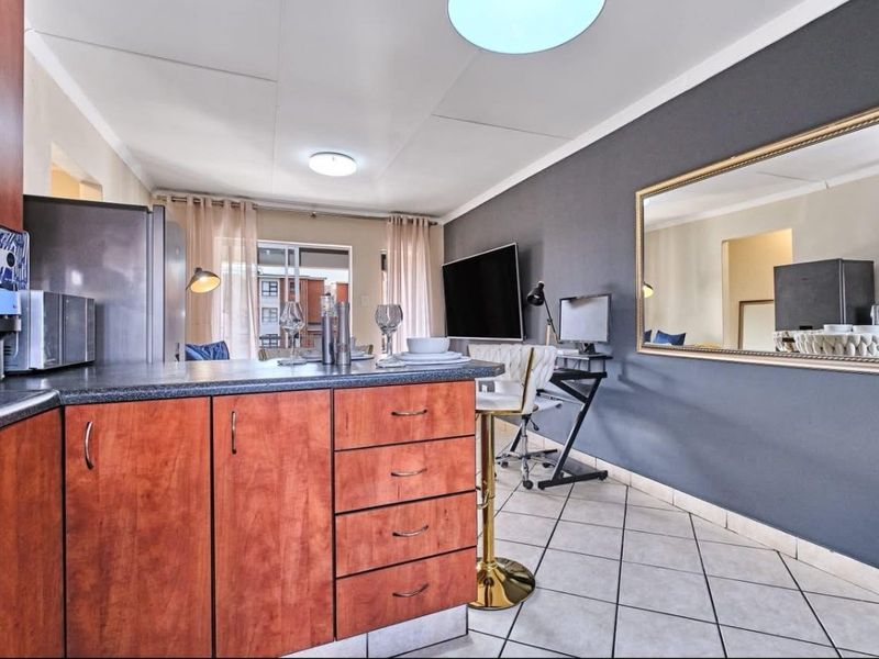 Open-plan living area featuring a kitchen with laminate cabinetry and tiled flooring, leading to a balcony through sliding glass doors.