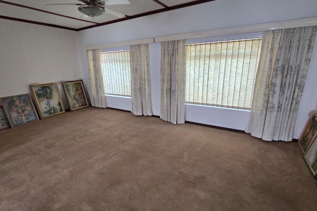Spacious living room featuring neutral carpeting, ceiling fan, and large windows with vertical blinds, offering a blank canvas for potential interior updates.