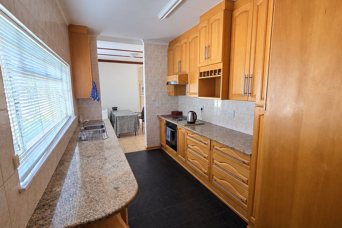 A functional kitchen featuring wooden cabinetry, granite countertops, a double basin sink, and built-in cooking appliances with tiled finishes.