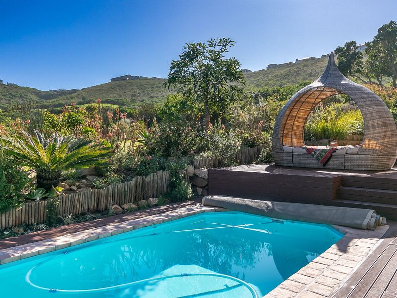 A well-maintained swimming pool area featuring timber decking, a pool cover, and a landscaped garden with mountain views.