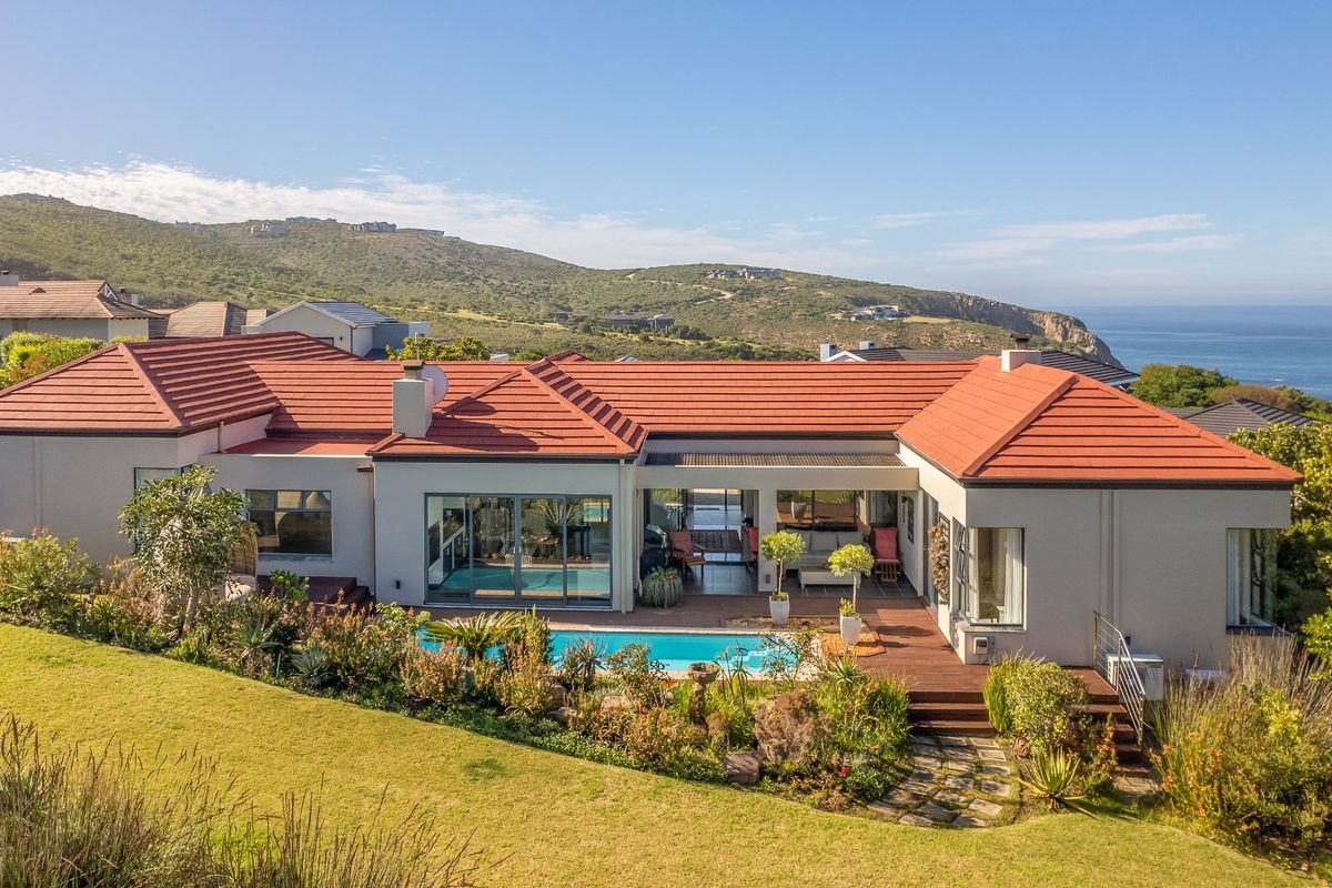 Rear view of a well-maintained residence featuring a swimming pool, timber decking, and landscaped gardens with scenic coastal and mountain views.