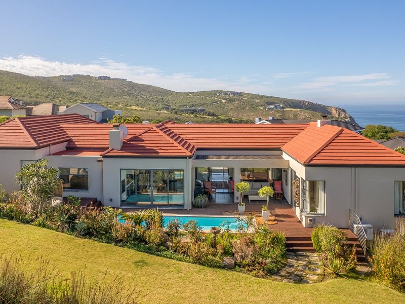 Rear view of a well-maintained residence featuring a swimming pool, timber decking, and landscaped gardens with scenic coastal and mountain views.