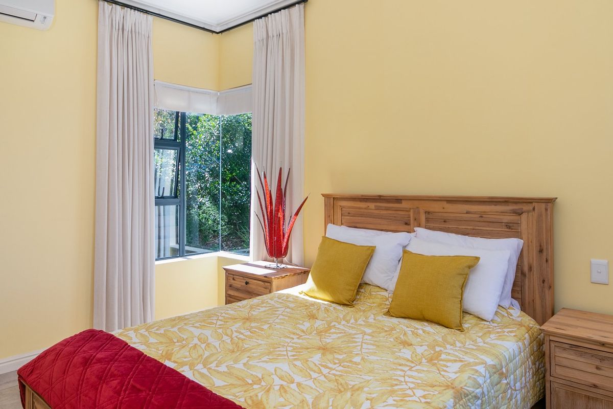 A bright bedroom featuring a corner window, neutral walls, and a wall-mounted air conditioning unit.
