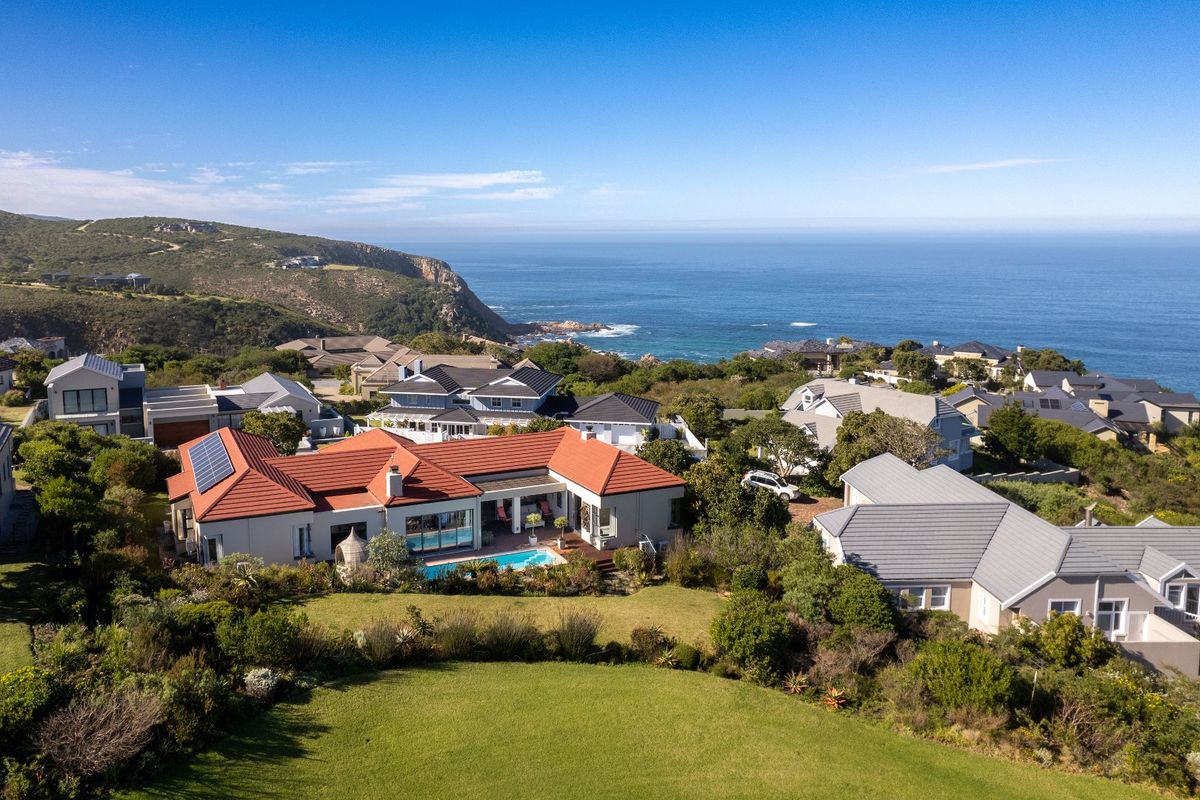 Aerial view of a coastal residential property featuring a swimming pool, landscaped garden, and solar panels, set against a scenic ocean backdrop.