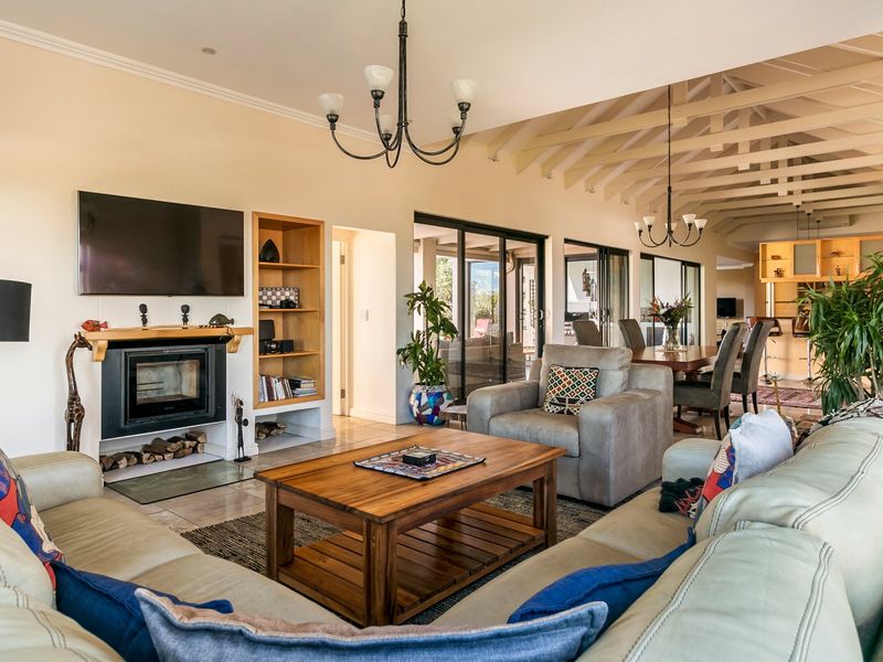 Spacious open-plan living and dining area featuring exposed timber beams, a cozy fireplace, built-in shelving, and large sliding doors leading to the patio.