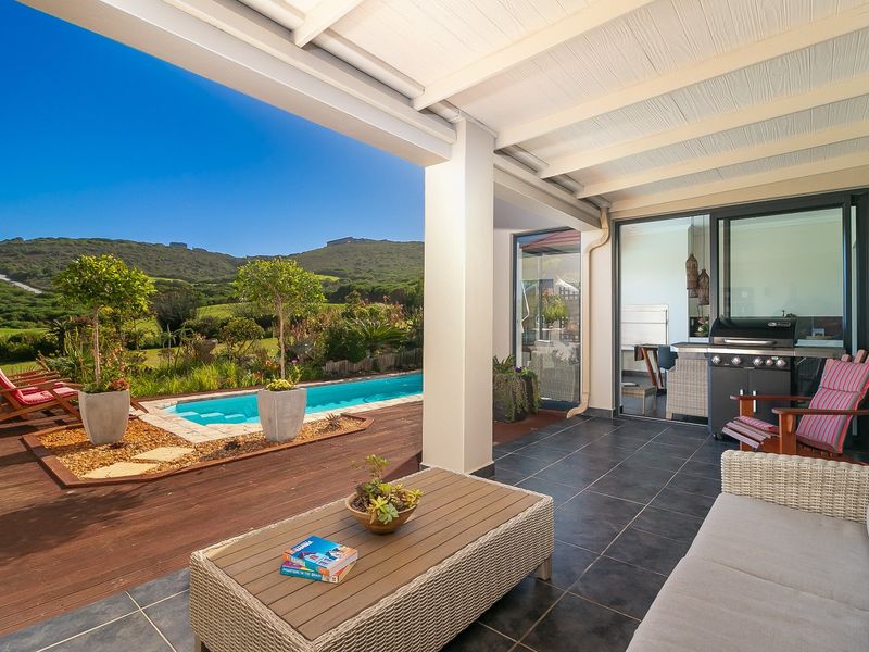 A spacious covered patio featuring tiled flooring, overlooking a swimming pool, timber decking, and scenic landscape views.