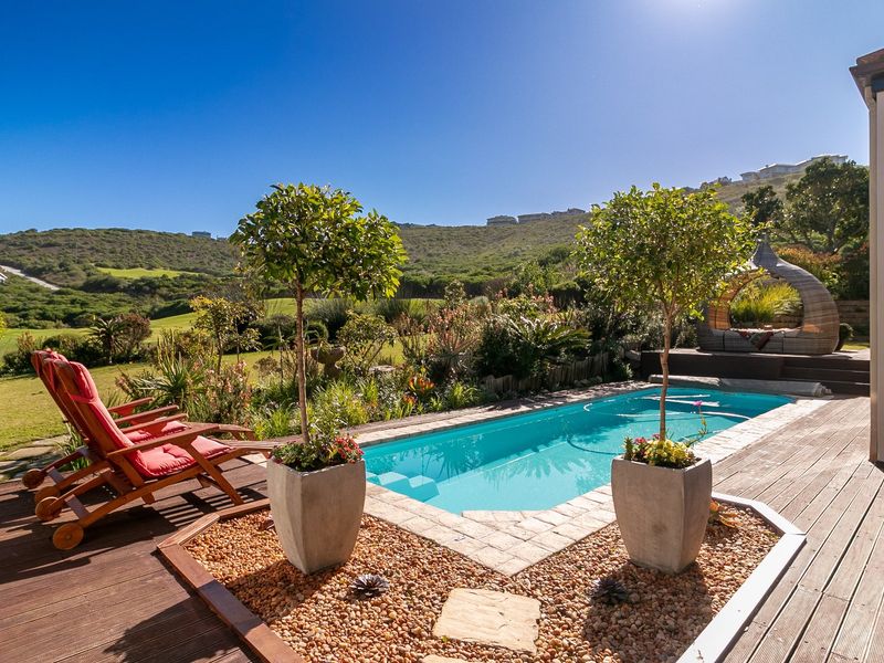 A beautifully maintained outdoor pool area featuring timber decking, stone paving, and a landscaped garden with scenic hillside views.