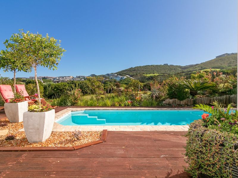 A well-maintained outdoor pool area featuring timber decking, stone coping, and a landscaped garden with scenic hillside views.