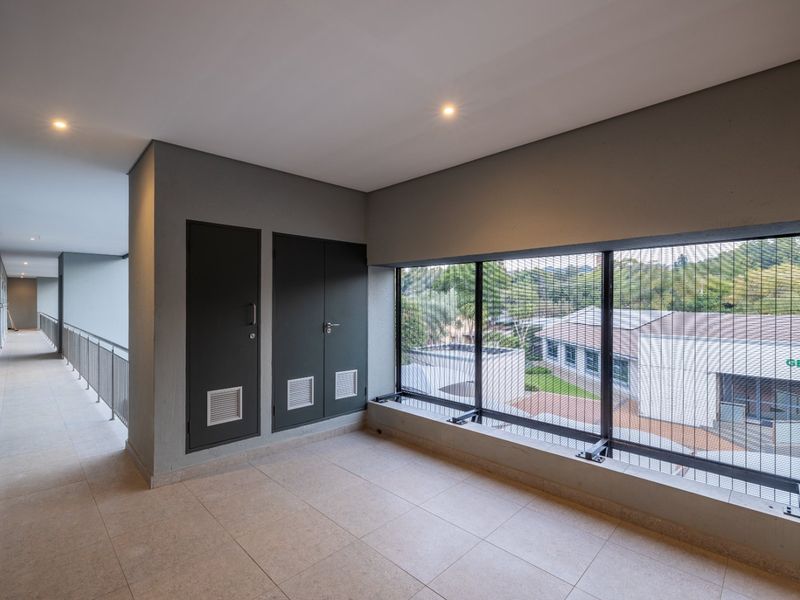 A modern, well-maintained commercial hallway featuring tiled flooring, recessed lighting, built-in utility cupboards, and large windows with integrated security mesh.
