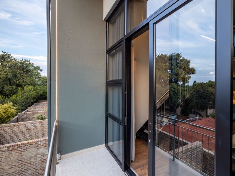 A modern balcony featuring tiled flooring, a sleek metal railing, and a large sliding glass door providing access to the interior.