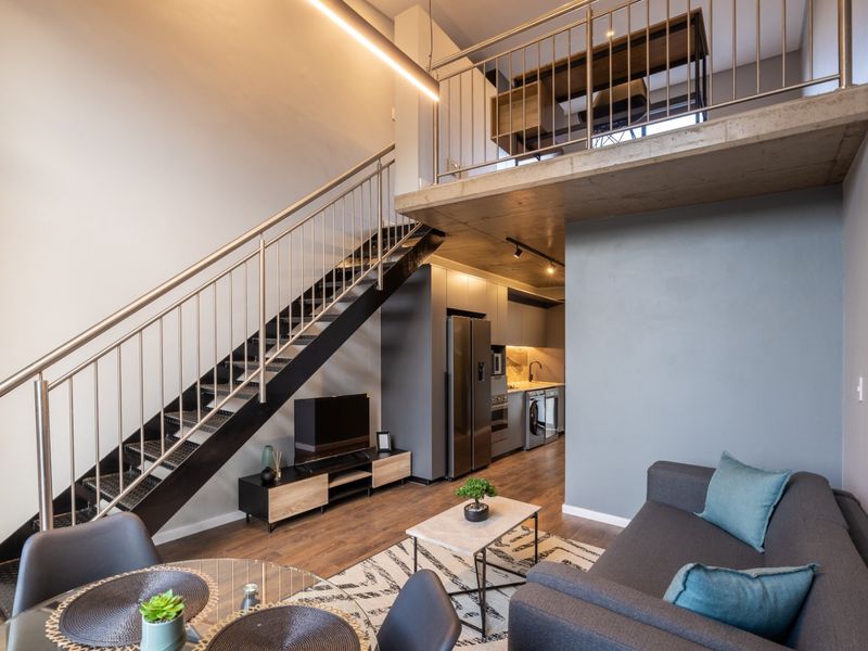 Modern open-plan living area featuring a mezzanine level, sleek kitchen cabinetry, and a contemporary metal staircase with stainless steel railings.