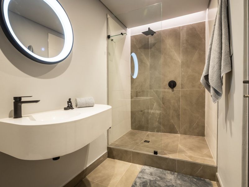Modern bathroom featuring a wall-mounted vanity, LED backlit mirror, and a spacious walk-in shower with contemporary black fixtures and large-format porcelain tiling.