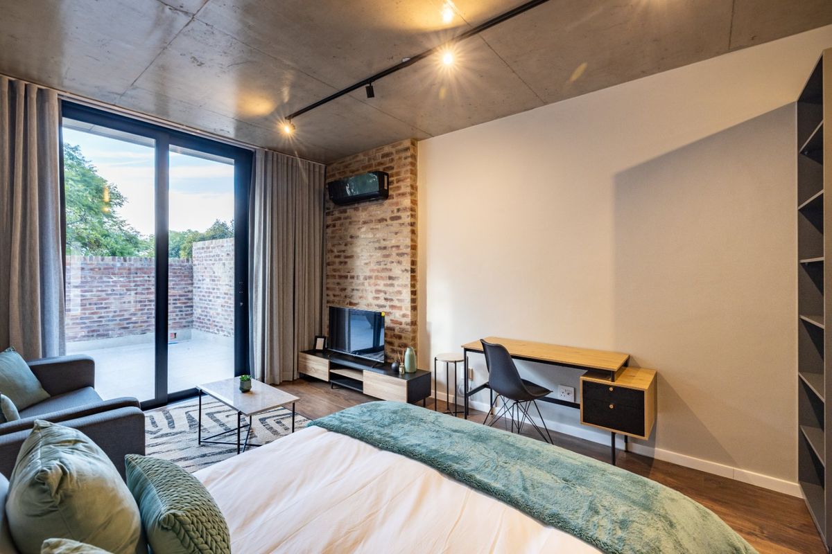 Modern bedroom featuring an exposed concrete ceiling, brick feature wall, and large sliding glass doors leading to a private patio area.