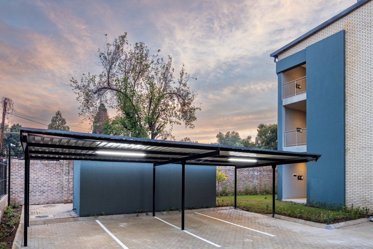 A well-maintained commercial parking area featuring a modern steel carport structure, paved surfacing, and exterior lighting adjacent to a multi-story building.