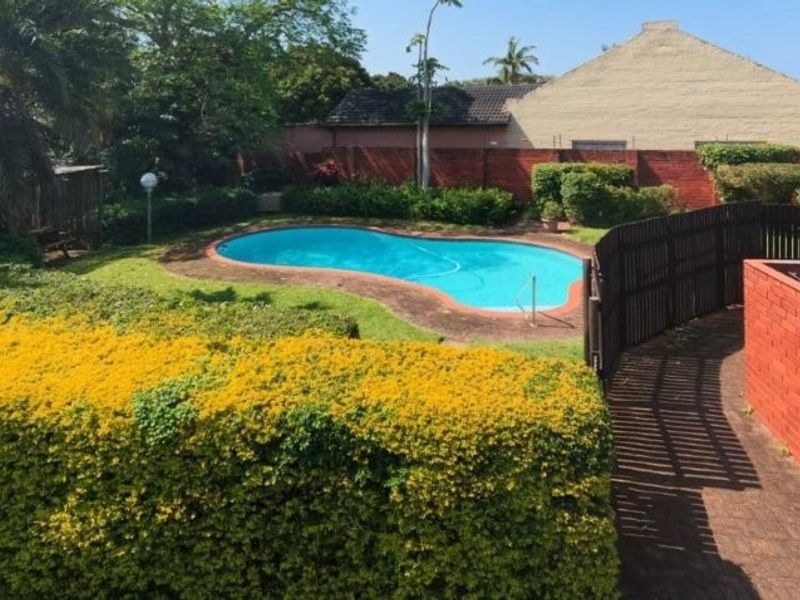 An elevated view of a private swimming pool set within a landscaped garden, featuring brick boundary walls and a paved walkway.