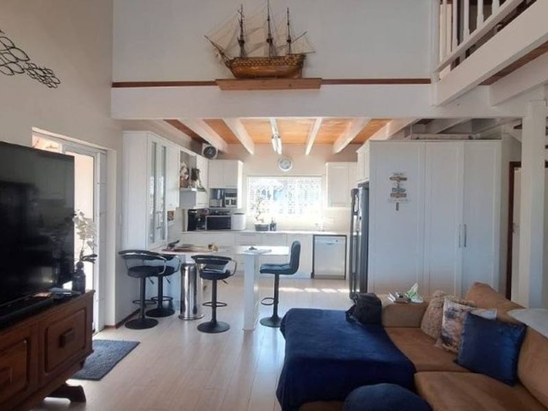 Open-plan living and kitchen area featuring exposed timber ceiling beams, a central kitchen island, and a staircase leading to an upper level.