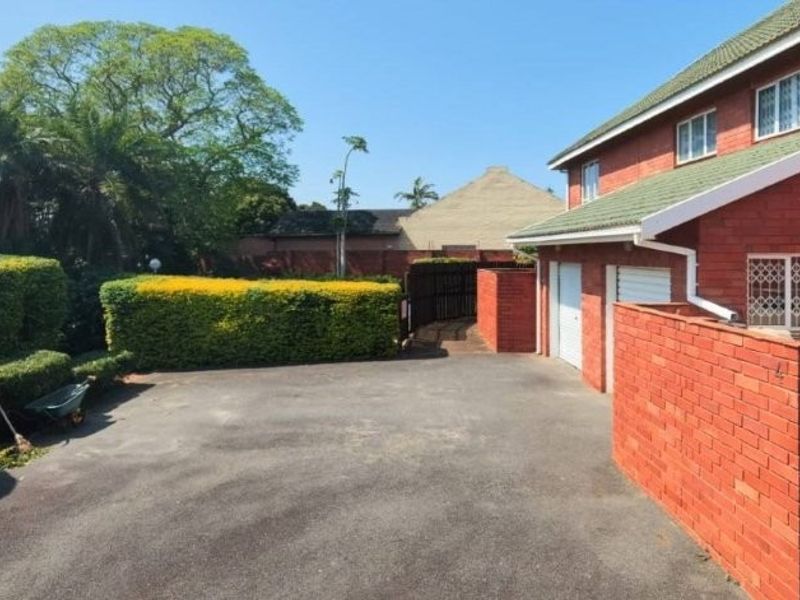 Front exterior view of a brick townhouse featuring a paved driveway, garage access, and established garden hedging.