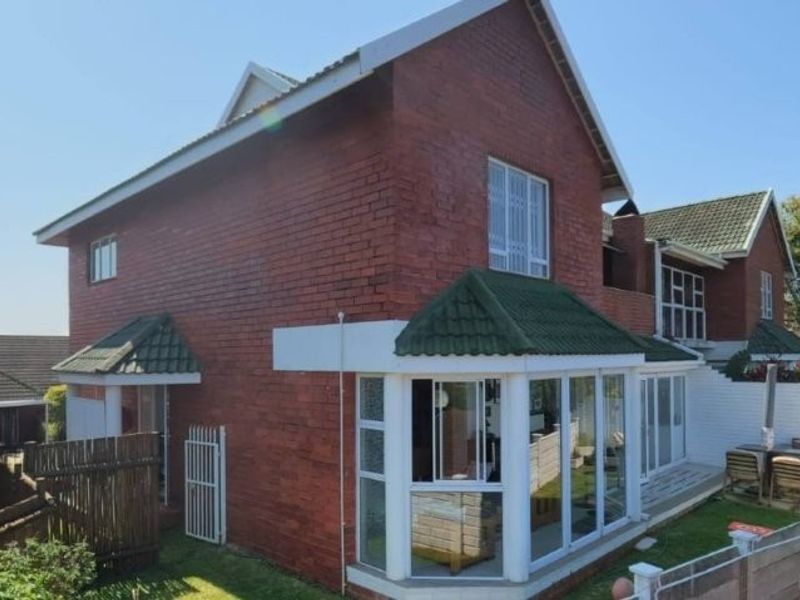 Rear view of a two-story red brick townhouse featuring a green tiled roof, a bay window, and a private garden area with electric fencing.