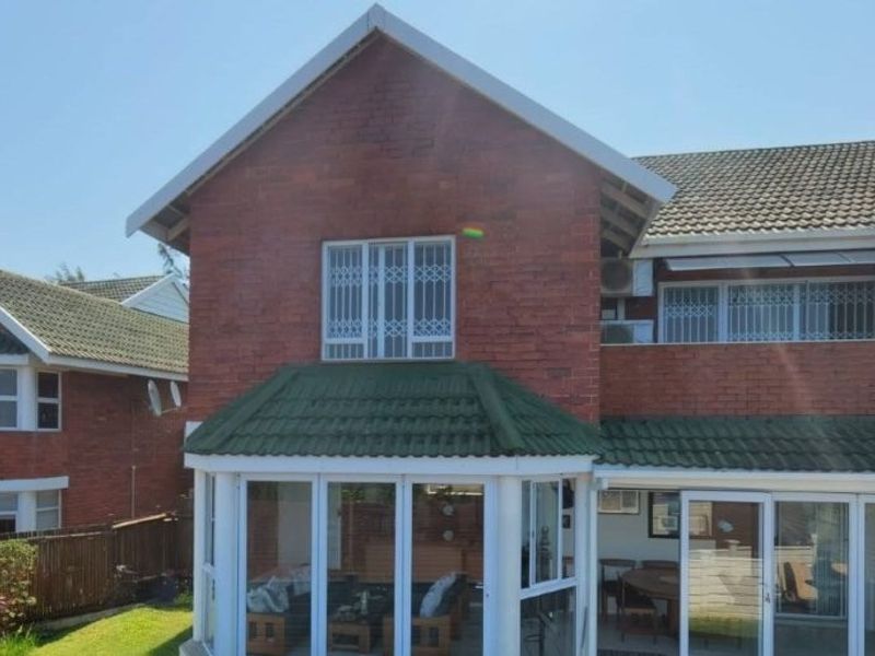 Rear view of a two-story townhouse featuring a brick facade, tiled roof, and ground-floor sunroom with large sliding glass doors.