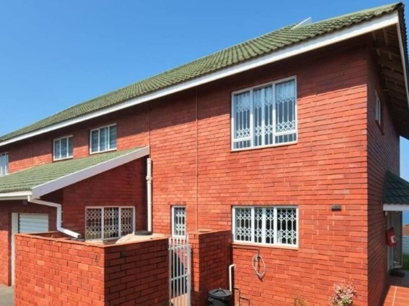 Rear view of a double-story face brick townhouse featuring a tiled roof, security bars on windows, and a paved patio area.
